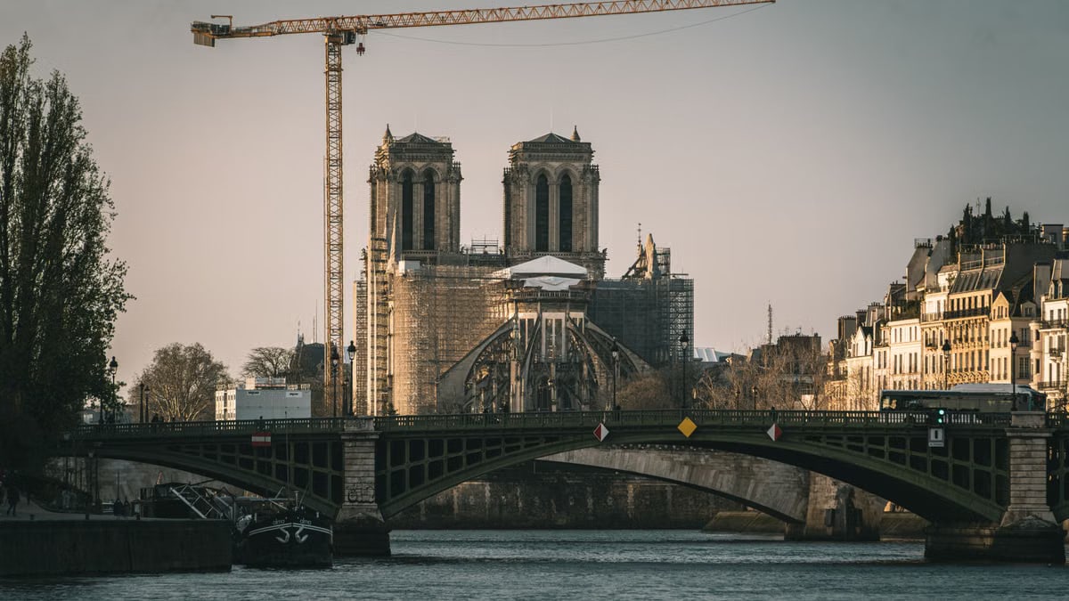 A view of Notre Dame Cathedral undergoing renovation with cranes over the Seine River in Paris.